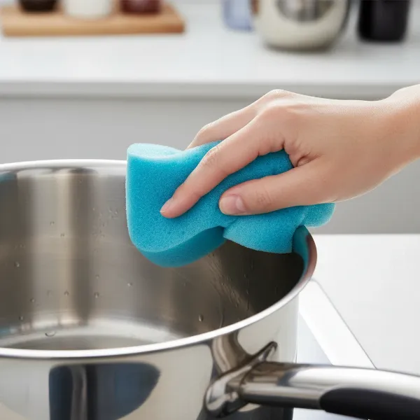 A hand gently cleaning a gleaming stainless steel pot with a soft sponge, illustrating proper maintenance for long-lasting cookware.